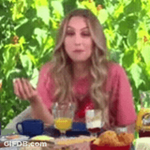 A Woman Is Sitting At A Table With A Glass Of Orange Juice And A Plate Of Food . GIF