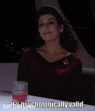 A Woman Is Sitting At A Table With A Glass Of Red Liquid And The Words It 'S Psychologically Valid GIF