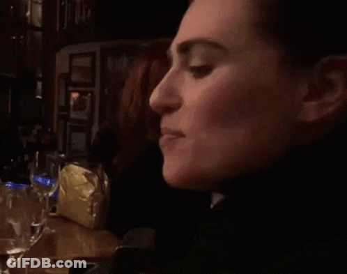 A Woman Is Sitting At A Table With A Glass Of Water In Front Of Her GIF