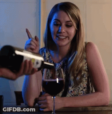 A Woman Is Sitting At A Table With A Glass Of Wine And A Bottle Of Wine Being Poured Into It GIF