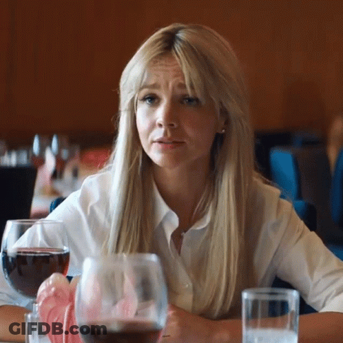 A Woman Is Sitting At A Table With A Glass Of Wine And A Glass Of Water . GIF