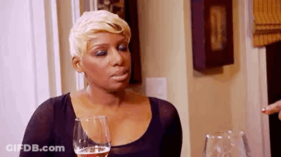 A Woman Is Sitting At A Table With A Glass Of Wine And Making A Funny Face . GIF