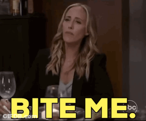 A Woman Is Sitting At A Table With A Glass Of Wine And Says " Bite Me " GIF