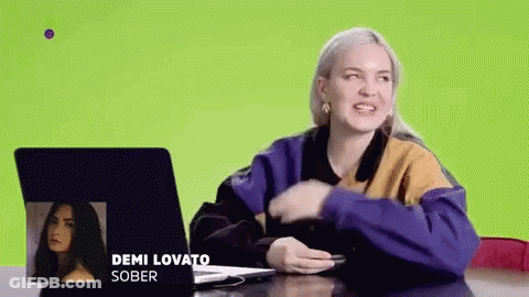 A Woman Is Sitting At A Table With A Laptop And A Picture Of Demi Lovato . GIF