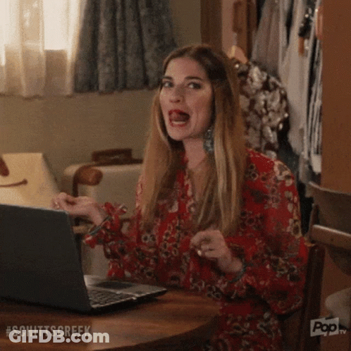 A Woman Is Sitting At A Table With A Laptop Computer And Making A Funny Face . GIF