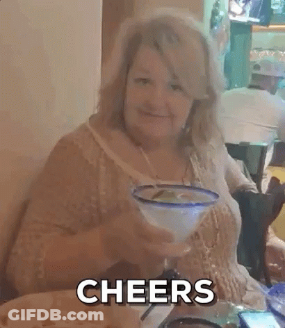 A Woman Is Sitting At A Table With A Margarita In Her Hand And The Words Cheers Behind Her . GIF