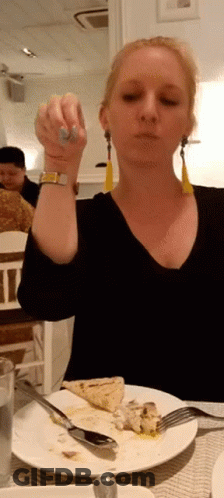 A Woman Is Sitting At A Table With A Plate Of Food And A Fork In Her Hand GIF