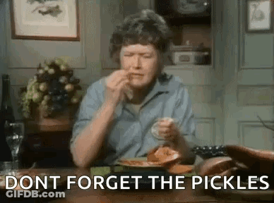 A Woman Is Sitting At A Table With A Plate Of Food And Pickles . GIF
