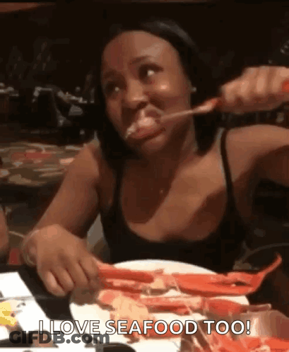 A Woman Is Sitting At A Table With A Plate Of Seafood And Eating It . GIF