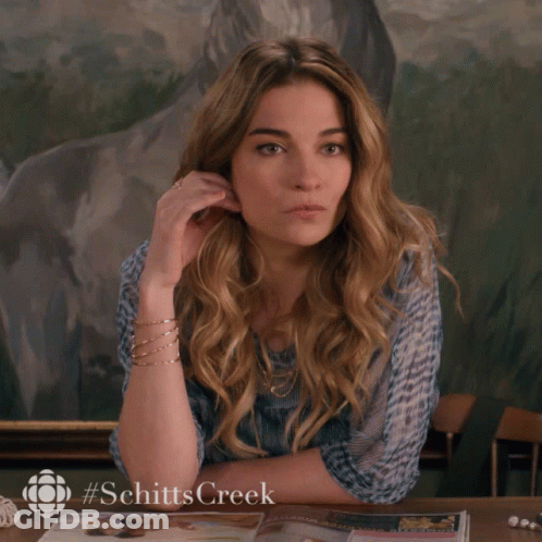 A Woman Is Sitting At A Table With A #Schittscreek Logo On The Bottom GIF
