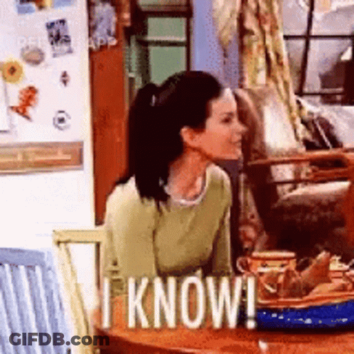 A Woman Is Sitting At A Table With A Sign That Says I Know ! GIF