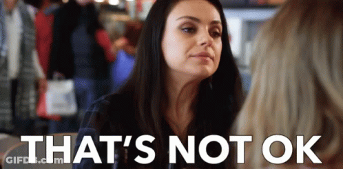 A Woman Is Sitting At A Table With A Sign That Says `` That 'S Not Ok '' GIF