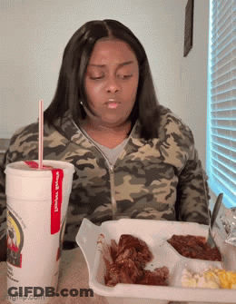 A Woman Is Sitting At A Table With A Tray Of Food And A Cup That Says James ' Place GIF