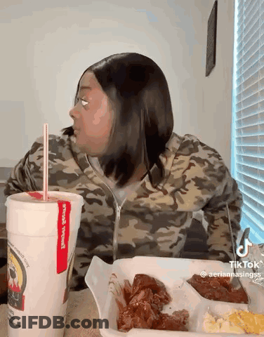 A Woman Is Sitting At A Table With A Tray Of Food And A Drink . GIF