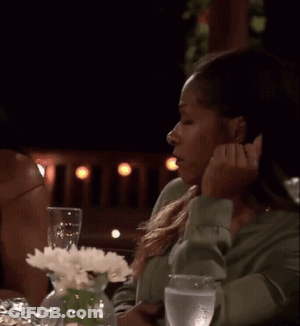 A Woman Is Sitting At A Table With A Vase Of Flowers And Glasses Of Water . GIF