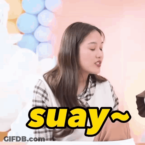 A Woman Is Sitting At A Table With Balloons In The Background And The Word Suay In Yellow Letters GIF