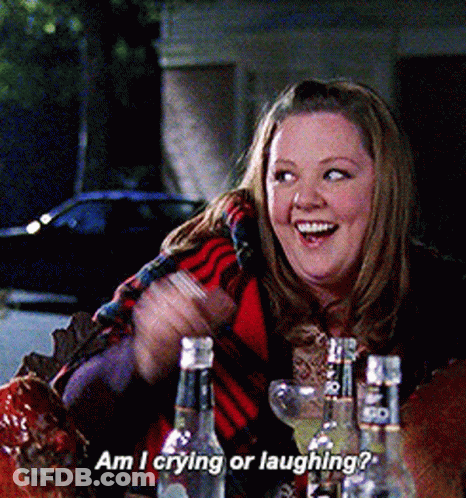 A Woman Is Sitting At A Table With Bottles Of Liquor And Says Am I Crying Or Laughing GIF