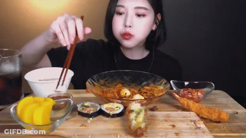 A Woman Is Sitting At A Table With Chopsticks Eating Food GIF