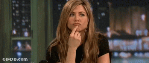 A Woman Is Sitting At A Table With Her Finger On Her Chin And Making A Funny Face . GIF