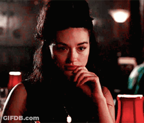 A Woman Is Sitting At A Table With Her Hand On Her Face GIF