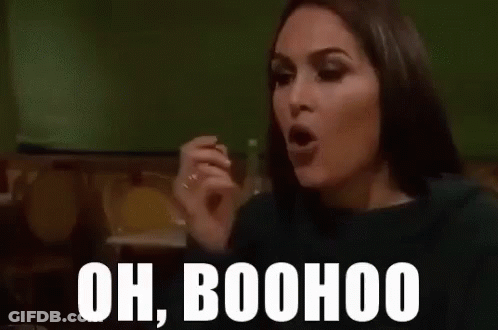 A Woman Is Sitting At A Table With Her Hand Up And The Words `` Oh Boohoo '' Written On Her Face . GIF
