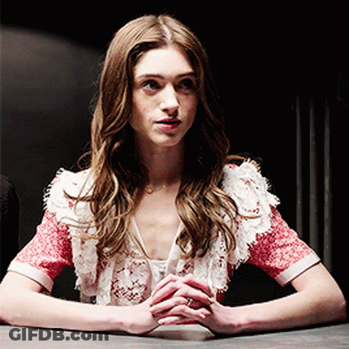 A Woman Is Sitting At A Table With Her Hands Folded In Front Of Her GIF