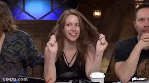 A Woman Is Sitting At A Table With Her Hands In Her Hair While A Man Looks On . GIF