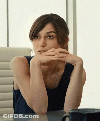A Woman Is Sitting At A Table With Her Hands On Her Chin GIF