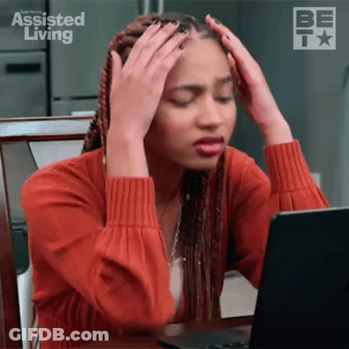 A Woman Is Sitting At A Table With Her Hands On Her Head While Looking At A Laptop Computer . GIF
