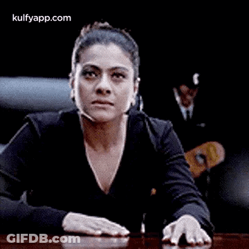 A Woman Is Sitting At A Table With Her Hands On The Table And Making A Funny Face . GIF