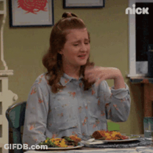 A Woman Is Sitting At A Table With Plates Of Food And A Nick Logo Behind Her GIF
