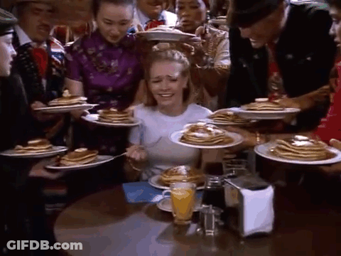 A Woman Is Sitting At A Table With Plates Of Pancakes And A Glass Of Orange Juice . GIF