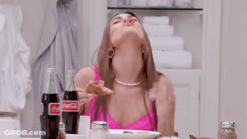 A Woman Is Sitting At A Table With Two Bottles Of Coca Cola GIF