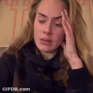 A Woman Is Sitting Down With Her Hand On Her Forehead And Making A Funny Face . GIF