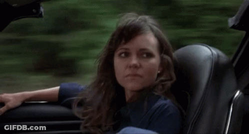 A Woman Is Sitting In A Car And Looking Out The Window . GIF