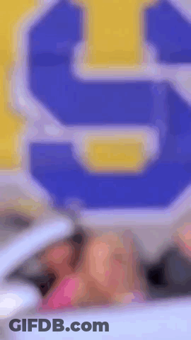 A Woman Is Sitting In A Car In Front Of A Blue And Yellow Sign That Says S. GIF