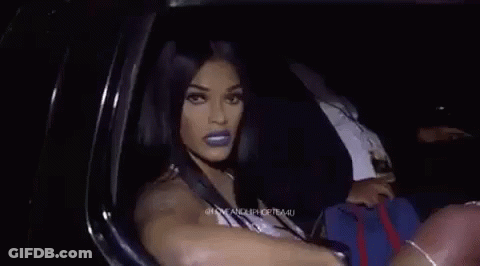 A Woman Is Sitting In A Car Making A Funny Face And Pointing At The Camera . GIF