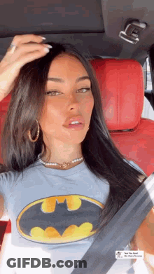 A Woman Is Sitting In A Car Wearing A Batman T-Shirt And Earrings . GIF