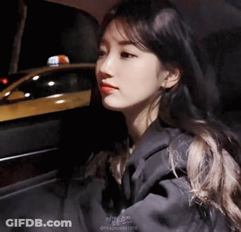 A Woman Is Sitting In A Car With A Taxi Cab In The Background GIF