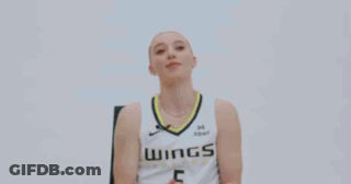 A Woman Is Sitting In A Chair And Smiling While Wearing A Basketball Uniform . GIF