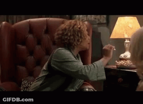 A Woman Is Sitting In A Chair Eating Popcorn Next To A Lamp And A Table . GIF
