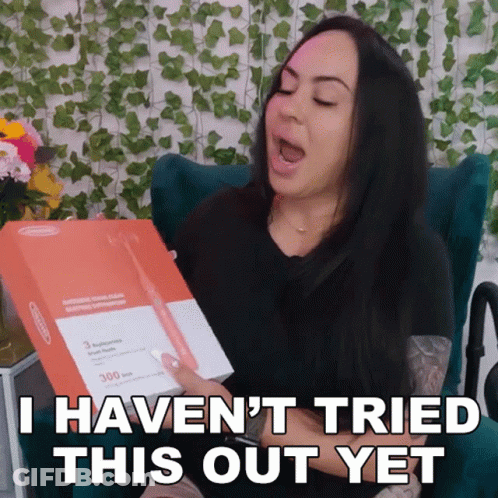 A Woman Is Sitting In A Chair Holding A Box That Says " I Haven 'T Tried This Out Yet " GIF