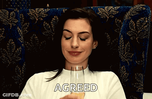 A Woman Is Sitting In A Chair Holding A Glass Of Champagne And The Word Agreed Is On The Bottom Of Her Shirt GIF