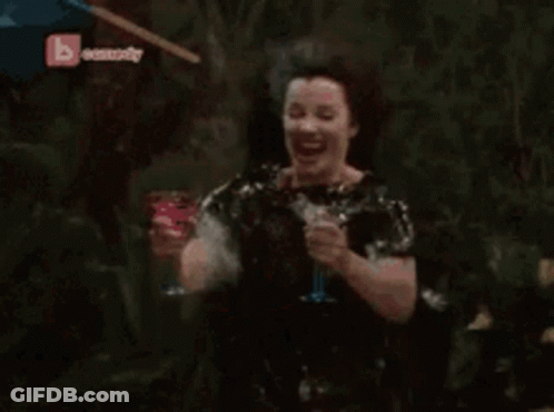 A Woman Is Sitting In A Chair In A Garden With A B Comedy Logo In The Corner GIF