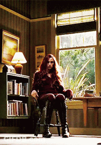 A Woman Is Sitting In A Chair In Front Of A Bookshelf GIF