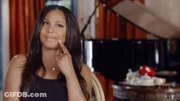 A Woman Is Sitting In A Chair In Front Of A Piano And Pointing To Her Face . GIF