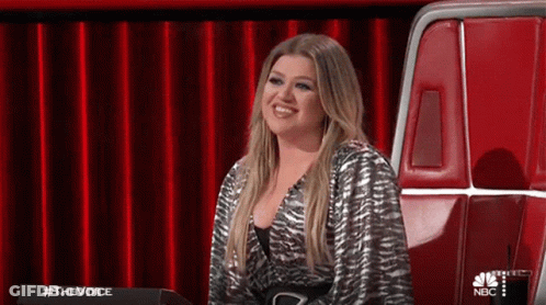 A Woman Is Sitting In A Chair In Front Of A Red Curtain On A Stage . GIF