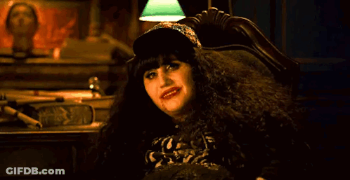 A Woman Is Sitting In A Chair Making A Devil Horns Sign With Her Hand . GIF