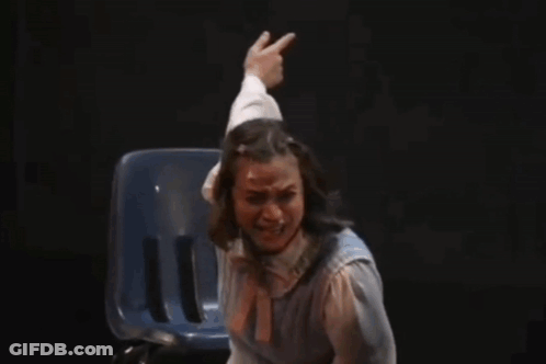 A Woman Is Sitting In A Chair On A Stage While A Man Reaches Out To Her . GIF