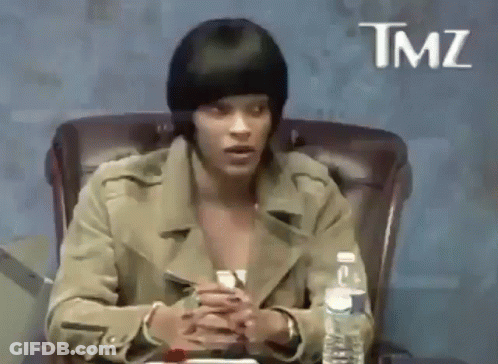 A Woman Is Sitting In A Chair With A Bottle Of Water In Front Of Her And A Sign That Says Tmz . GIF